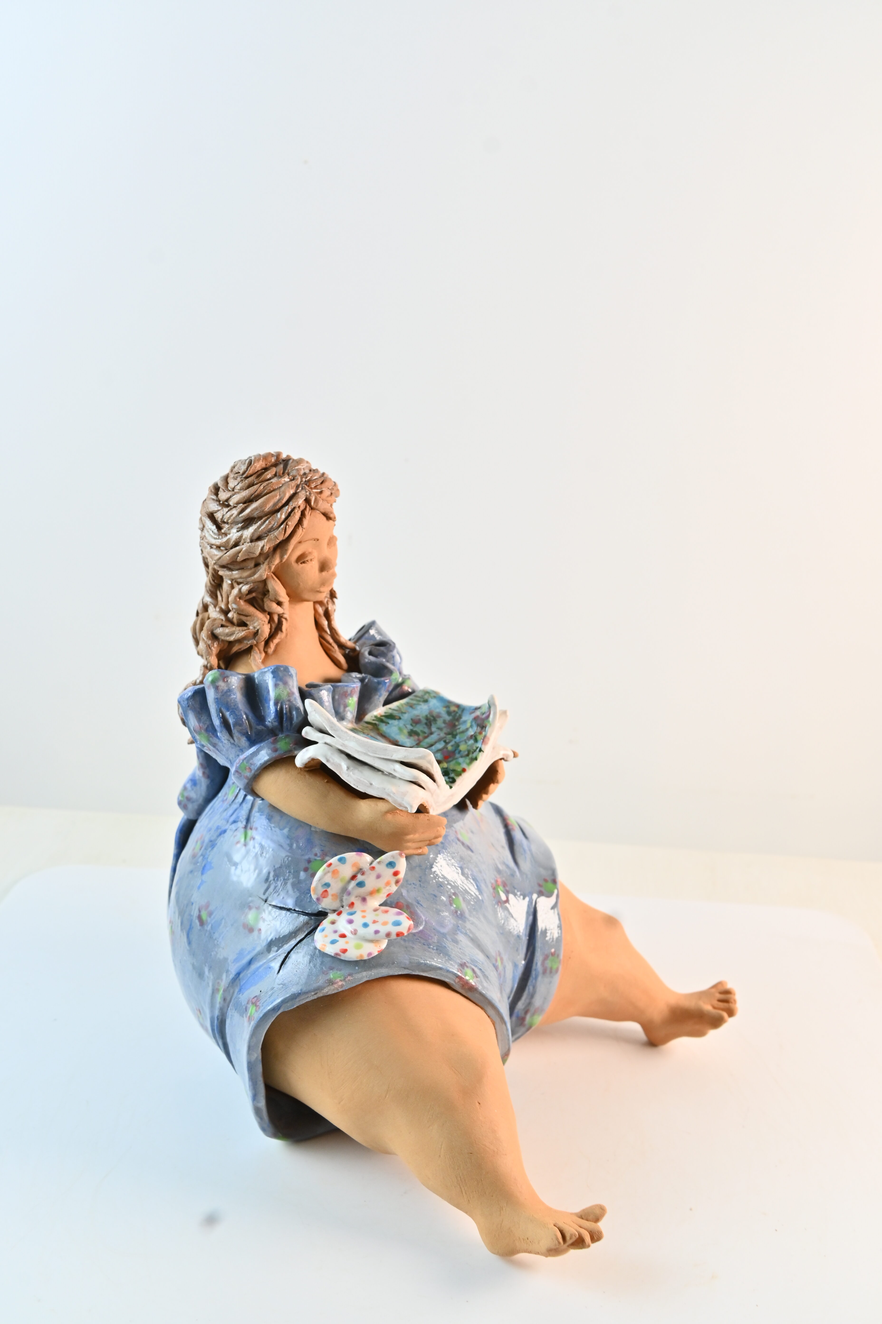 Ceramic sculpture of a seated woman reading an open book in a blue dress