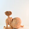 Scultura lettrice in ceramica distesa sul fianco con libro aperto e abito a pois azzurri e rosa
